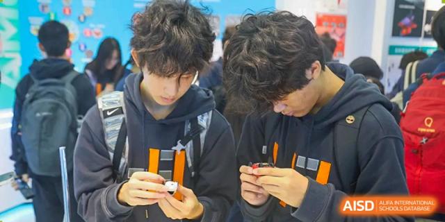 Two students lean in closely to examine and manipulate small mechanical components or electronic parts during a workshop at Huafu International Department.