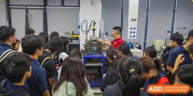An instructor in a red shirt demonstrates industrial machinery or a scientific apparatus to a seated group of students at Huafu International Department.