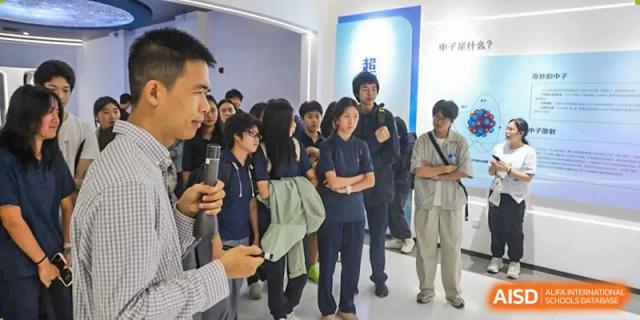 A large group of students in school uniforms gathers in a hallway to listen to a guided tour or an educational presentation at Huafu International Department.