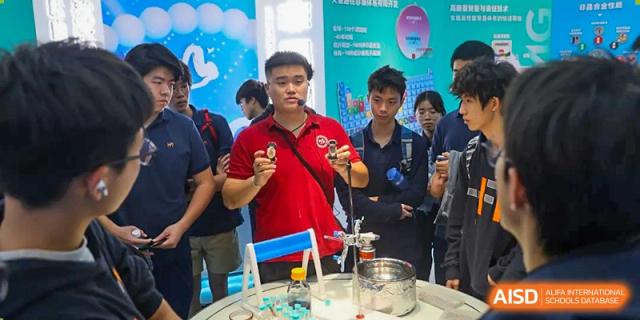 A student presenter wearing a microphone leads a science demonstration with laboratory equipment for his peers at Huafu International Department.