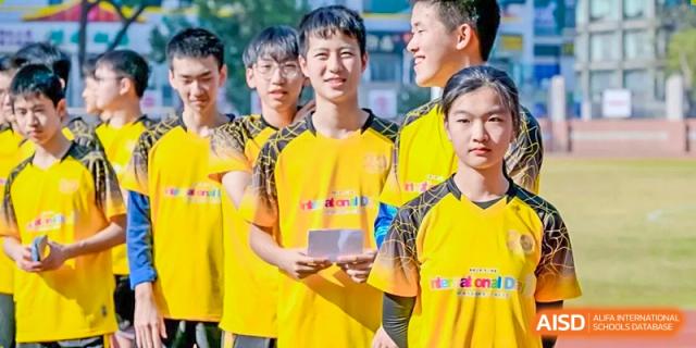 A group of smiling students in yellow and black soccer jerseys stand together on the field, with one holding a card, during a sports event at the Huafu International Department.