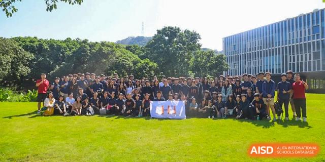 Large group of students in navy uniforms posing with a banner on a green lawn under a bright sky, showcasing school spirit at the Huafu International Department.