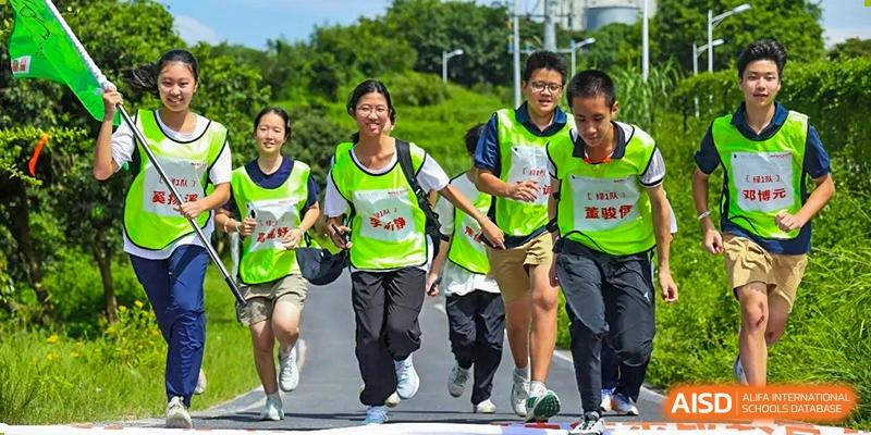Students wearing bright neon yellow safety vests jogging along a paved path during an outdoor fitness activity at the Huafu International Department.