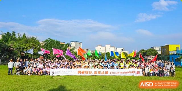 Students gathered behind a large horizontal banner on a grassy field with colorful flags flying in the background at the Huafu International Department.