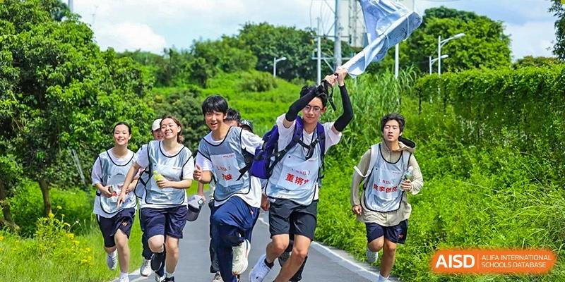 A young man in a sports vest runs enthusiastically while waving a blue flag during an outdoor school marathon at the Huafu International Department.