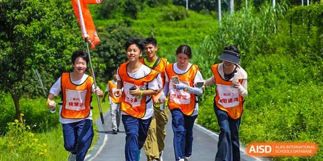 A group of students wearing orange numbered racing bibs running together down a scenic road during a school race at the Huafu International Department.