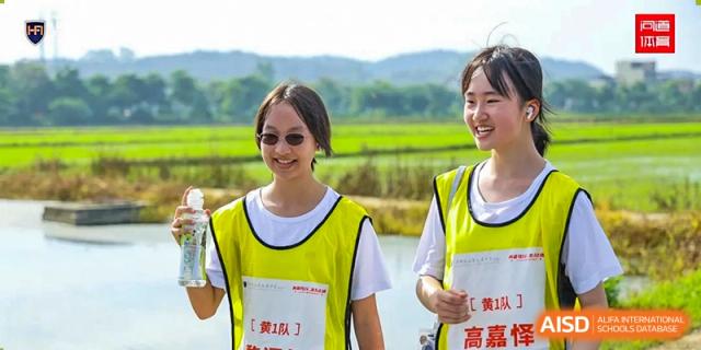 A smiling student wearing a yellow vest and sunglasses participates in an outdoor team-building event near a rural field at the Huafu International Department.