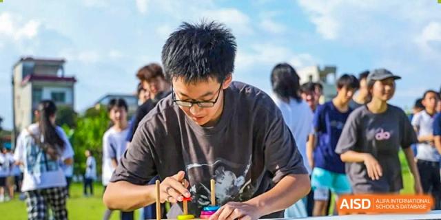 A student concentrates intensely while playing a tabletop game involving stacking rings during a school festival at the Huafu International Department.