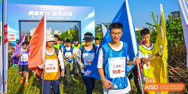 A group of students walks through an outdoor event entrance, wearing athletic gear and identification bibs for a school-wide hiking or trekking expedition at Huafu International Department.