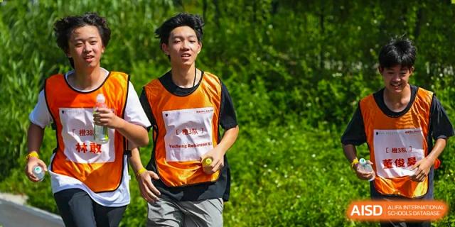 A male student in an orange athletic vest runs outdoors during a bright, sunny day, showcasing fitness and school spirit during a competitive race at Huafu International Department.