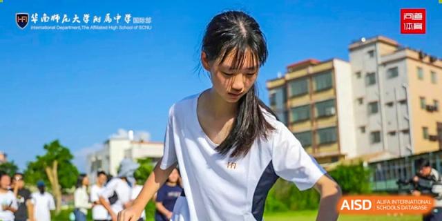 A close-up of a female student in a white athletic shirt looking down thoughtfully while participating in a daytime outdoor sports or orientation event at Huafu International Department.