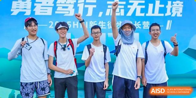 Three male students stand together with raised fists and smiles, celebrating their successful completion of a challenging outdoor physical activity at Huafu International Department.