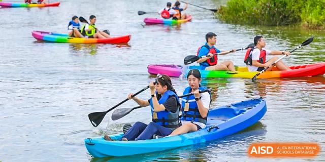 A group of students in blue life jackets paddle blue kayaks across a calm river, learning teamwork and water safety during an outdoor adventure at Huafu International Department.