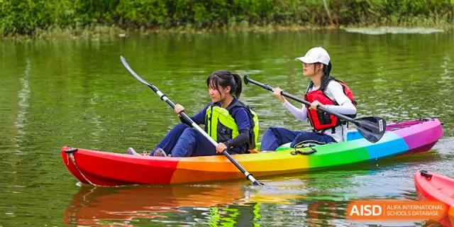 A female student sits in a colorful kayak on the water, holding an oar and wearing safety gear while participating in a supervised rowing session at Huafu International Department.