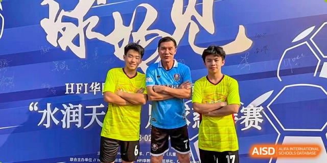 Two students and a coach pose together in athletic jerseys in front of a blue event backdrop, celebrating a sports milestone or competition for Huafu International Department.
