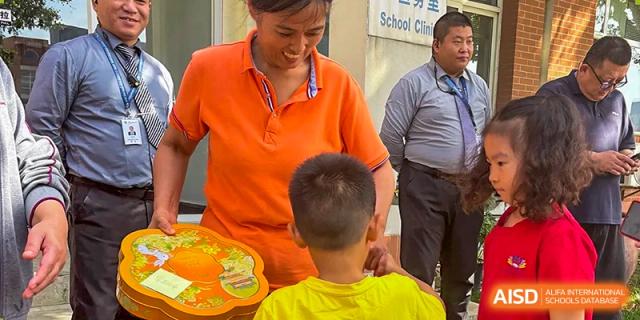 A teacher in an orange shirt interacts warmly with a student during an outdoor educational activity at TEDA International School Tianjin.