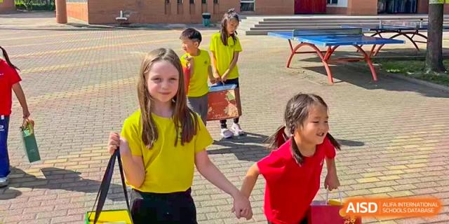 Students in bright yellow and red shirts hold hands while walking together on the school grounds at TEDA International School Tianjin.