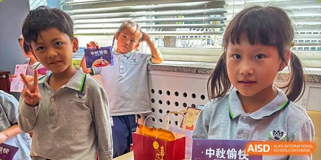 A student proudly shows off her artwork while standing near a window during a class project at TEDA International School Tianjin.