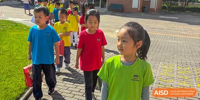 A line of students in colorful shirts walk together across the campus courtyard during the day at TEDA International School Tianjin.