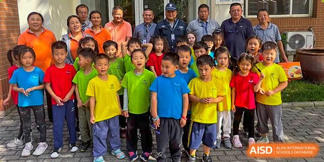 A large group of students in green and blue shirts poses for a photo with visiting community members at TEDA International School Tianjin.
