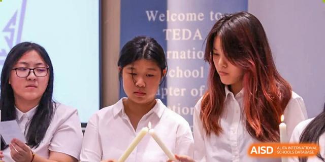Two female students in white shirts participate in a solemn candle-lighting ceremony during a formal event at TEDA International School Tianjin.