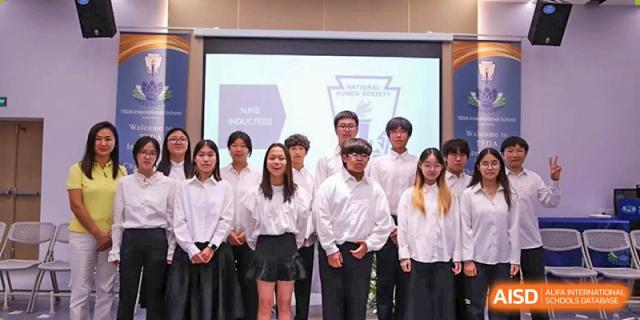 A group of students gather on stage for a formal induction ceremony in front of a digital presentation screen at TEDA International School Tianjin.