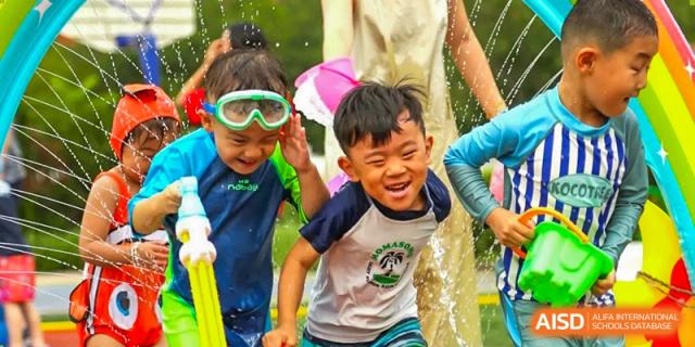 Two young boys laugh and play with water sprayers during an outdoor summer activity at TEDA International School Tianjin.