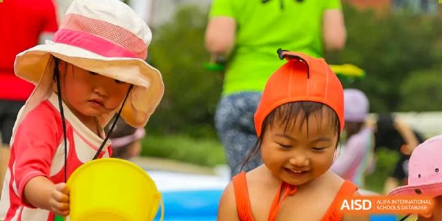 A young girl wearing a bright orange swim cap smiles while playing outdoors at TEDA International School Tianjin.