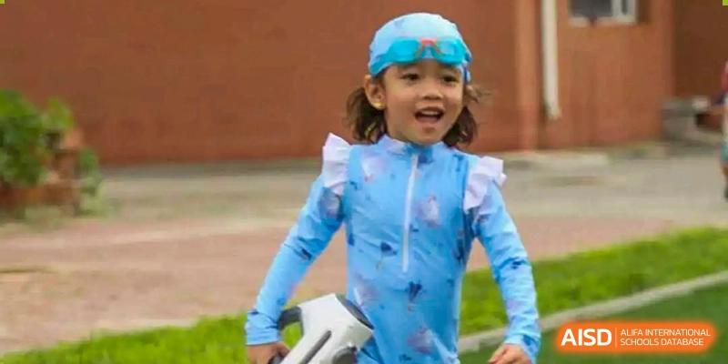 A happy young student in a blue swim shirt and goggles enjoys a water play day at TEDA International School Tianjin.