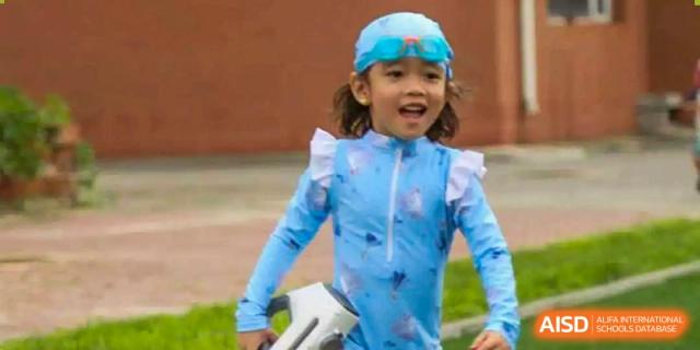 A happy young student in a blue swim shirt and goggles enjoys a water play day at TEDA International School Tianjin.
