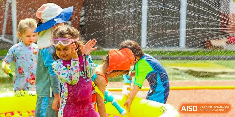 Students wearing swim gear play together in an outdoor water fountain area at TEDA International School Tianjin.