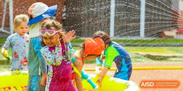 Students wearing swim gear play together in an outdoor water fountain area at TEDA International School Tianjin.