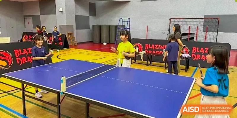 A female student stands ready at the end of a blue table tennis table during a sports session at TEDA International School Tianjin.