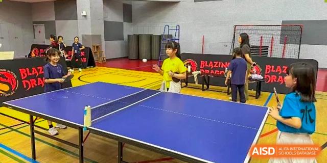 A female student stands ready at the end of a blue table tennis table during a sports session at TEDA International School Tianjin.