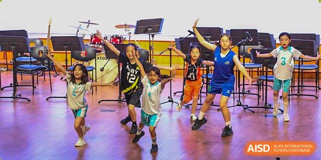 Young students in athletic wear perform a high-energy dance routine on a wooden stage at TEDA International School Tianjin.