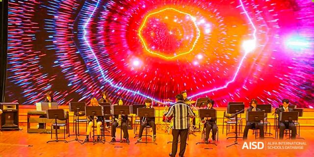A student orchestra performs on stage against a vibrant, glowing red and purple digital backdrop at TEDA International School Tianjin.