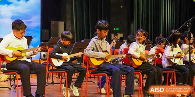 A group of students sit in a row while focused on playing acoustic guitars during a music showcase at TEDA International School Tianjin.