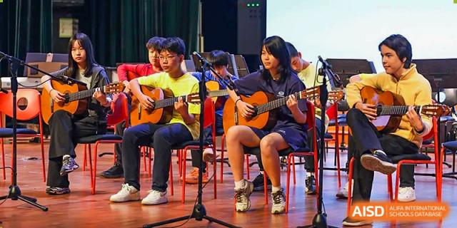 Female students play acoustic guitars together during a musical performance in the school auditorium at TEDA International School Tianjin.