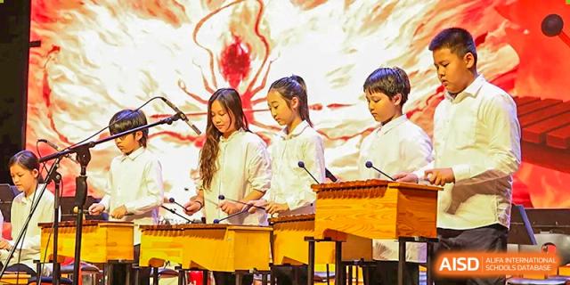 Three students play wooden xylophones with focus during a percussion ensemble performance at TEDA International School Tianjin.