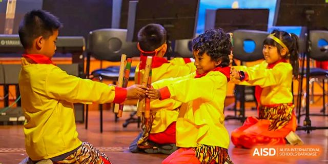 Students in bright yellow and red outfits perform a traditional cultural dance on stage at TEDA International School Tianjin.