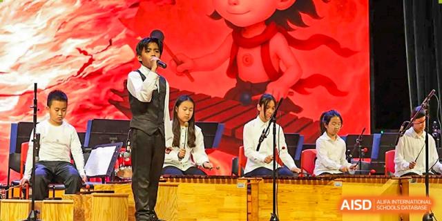 A young male student sings into a microphone while others play instruments behind him on stage at TEDA International School Tianjin.