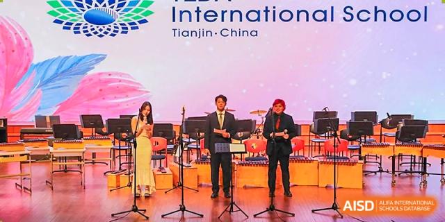 Three performers stand on a professional stage in front of the school's official digital logo at TEDA International School Tianjin.