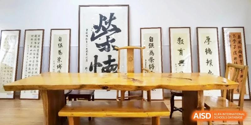 A traditional Chinese study room featuring a rustic wooden desk, calligraphy artwork in the background, and comfortable seating for cultural education at Ronghaui International School.