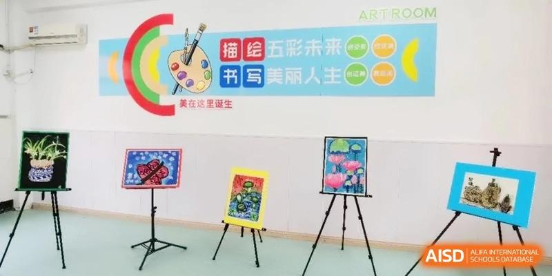An art room classroom featuring colorful student paintings displayed on easels, with a vibrant banner on the wall promoting creativity at Ronghaui International School.