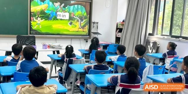 Students in blue chairs face a smartboard displaying an educational cartoon in a modern classroom setting at Ronghaui International School.