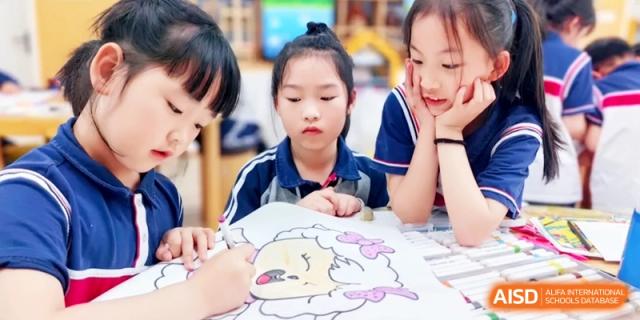 Three young children are focused on coloring a cartoon sheep drawing together at a wooden table in an art class at Ronghaui International School.