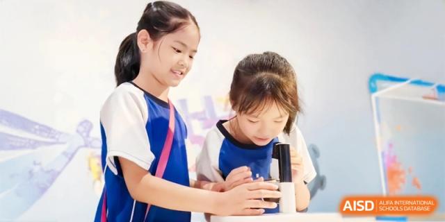 Two young students examine an item through a microscope together, conducting a science experiment in a bright lab at Ronghaui International School.