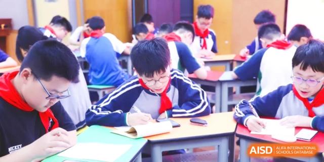 A classroom of students in school uniforms focused on their work, practicing writing and studying academic material diligently at Ronghaui International School.