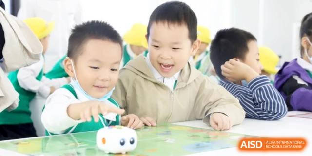 Students work together excitedly to program and operate a small, friendly-looking educational robot on a table surface at Ronghaui International School.