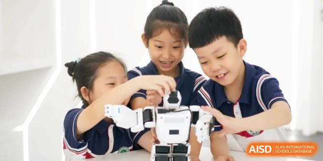 Young children joyfully collaborate to assemble a small white robot, developing teamwork and technical skills together at Ronghaui International School.
